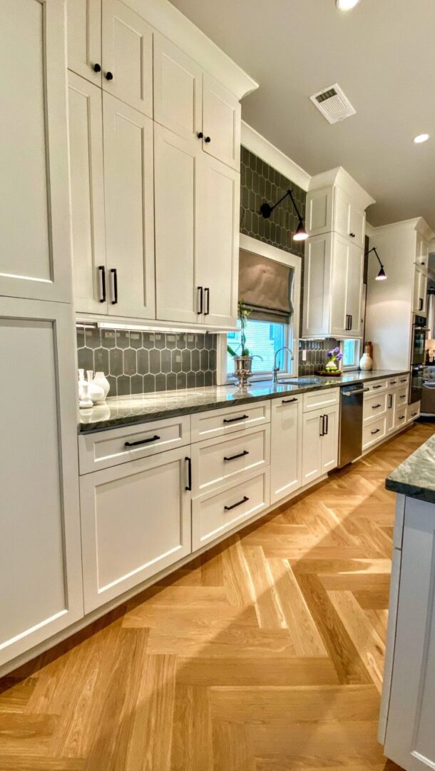 A kitchen with white cabinets and wood floors.