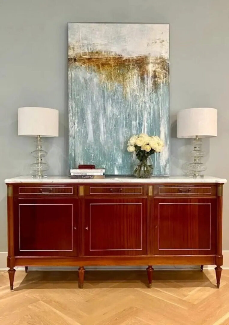 A large painting of flowers on the wall above a buffet.